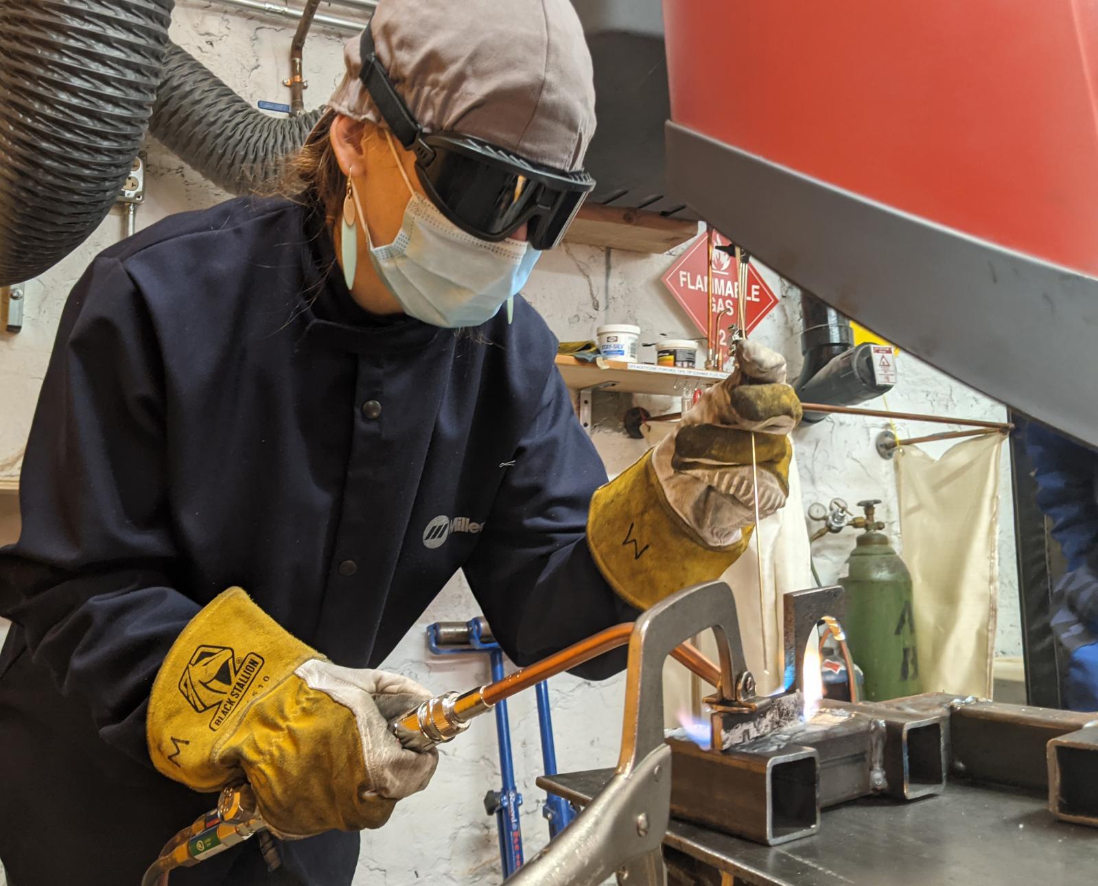 A MakeHaven member wearing her mask and other PPE welds